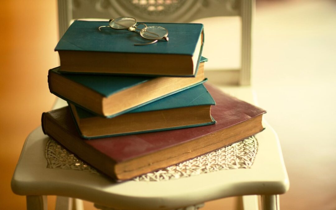 Stack of books on a chair with a pair of wire-framed glasses resting on the top book